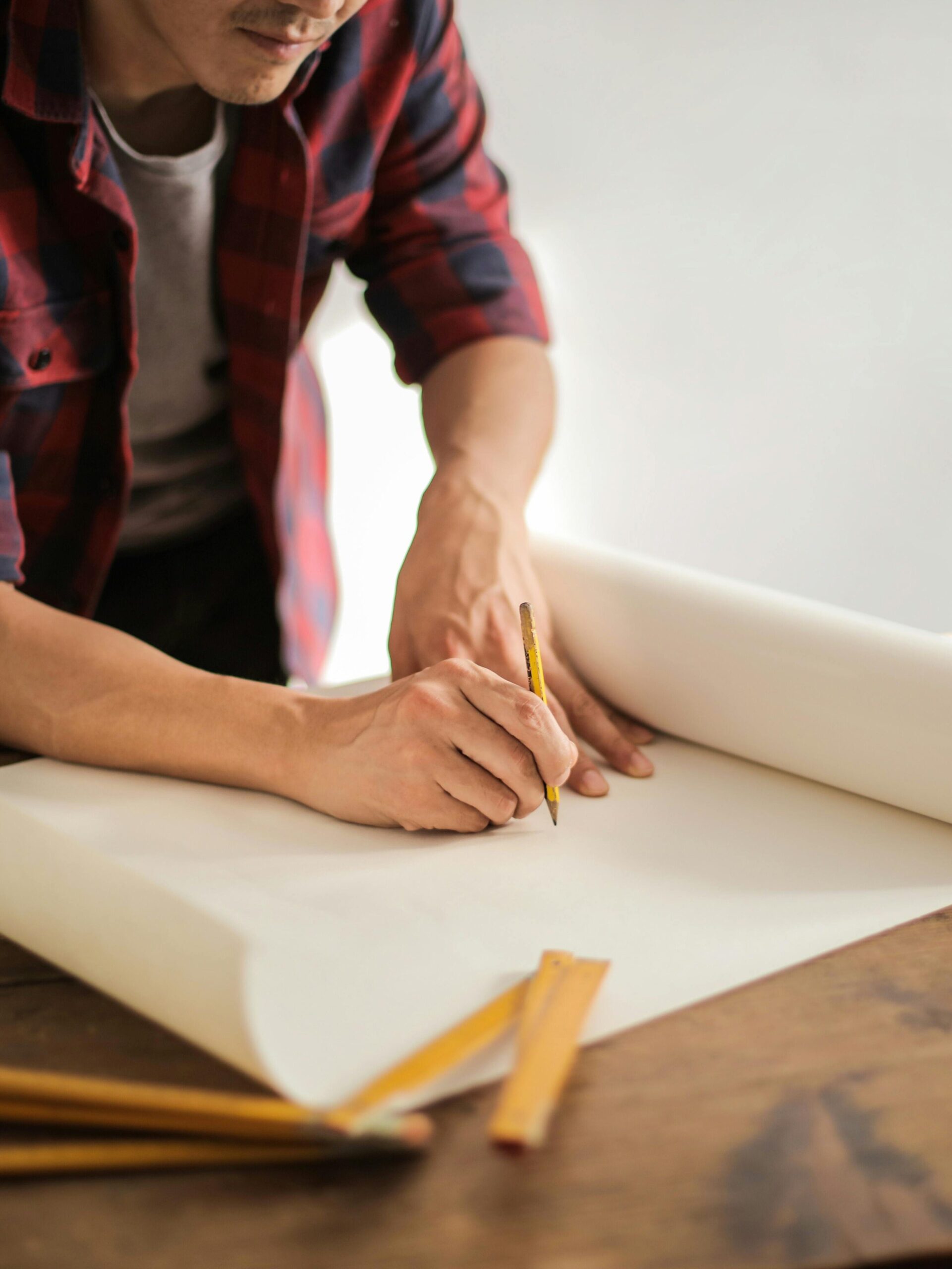 A focused architectural designer drafting blueprints at a desk indoors.